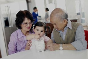 Asian grandparents sitting with granddaughter dropping coins in piggy bank