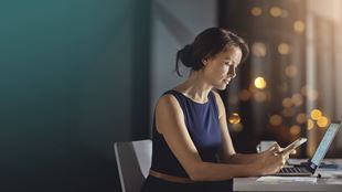 woman with phone and laptop at desk