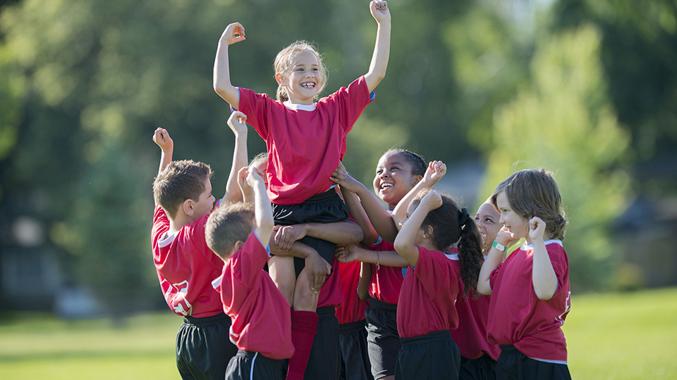 a young girl being stood up by her teammates to celebrate.