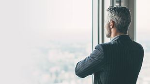 man looking out window with arms folded