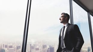 man looking out window in tall building