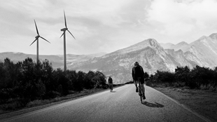 Cyclist on a paved road surrounded by wind turbines. 