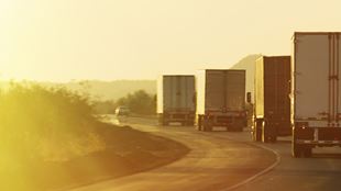 sun glowing over transport trucks on road