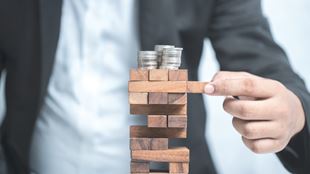 business person playing Jenga with money on top of game