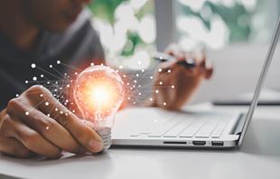 Men working at a computer is holding a lightbulb. 