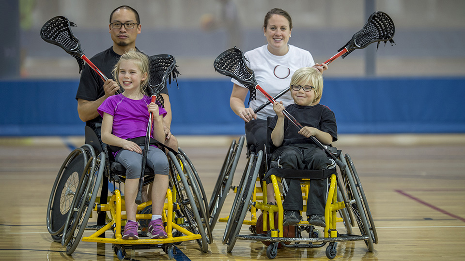 two children and two adults in wheelchairs playing lacrosse