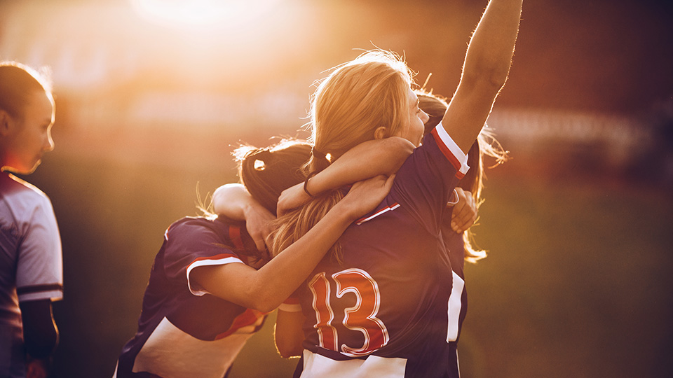 Des joueuses de soccer se font une accolades. L'une d'elle a son point lever en l'air en signe de célébration.